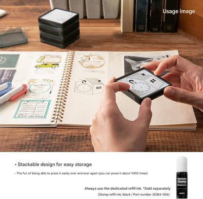 Person holding a small stackable stamp device over an open notebook with illustrations.